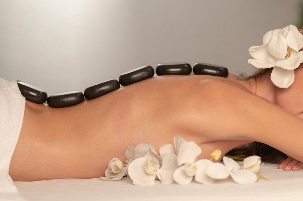 Serene spa image of hot stone therapy on a woman's back with white flowers, promoting relaxation.